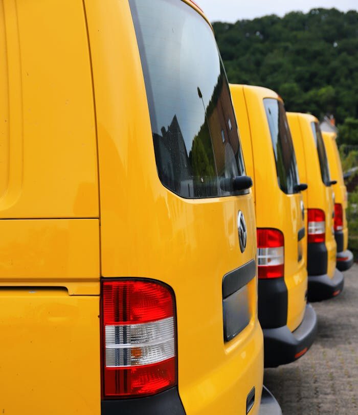 Bright yellow vans aligned in a parking lot outdoors, with lush greenery in the background.